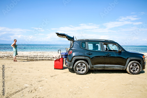 A woman in a hat and sunglasses and a car on a sunny sandy beach