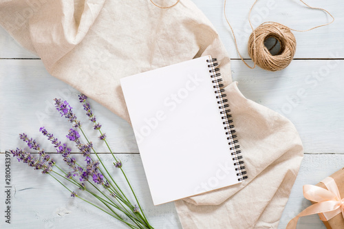 Stylish composition with lavender flowers, blank paper notepad mockup, pastel beige blanket, twine, gift box on rustic blue wooden desk table. Flat lay, top view, copy space.