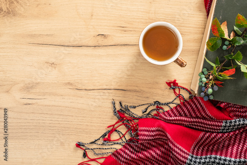 Book, knitted red scarf, cup of tea on wooden table. Flat lay, top view, copy space. Hygge autumn concept.
