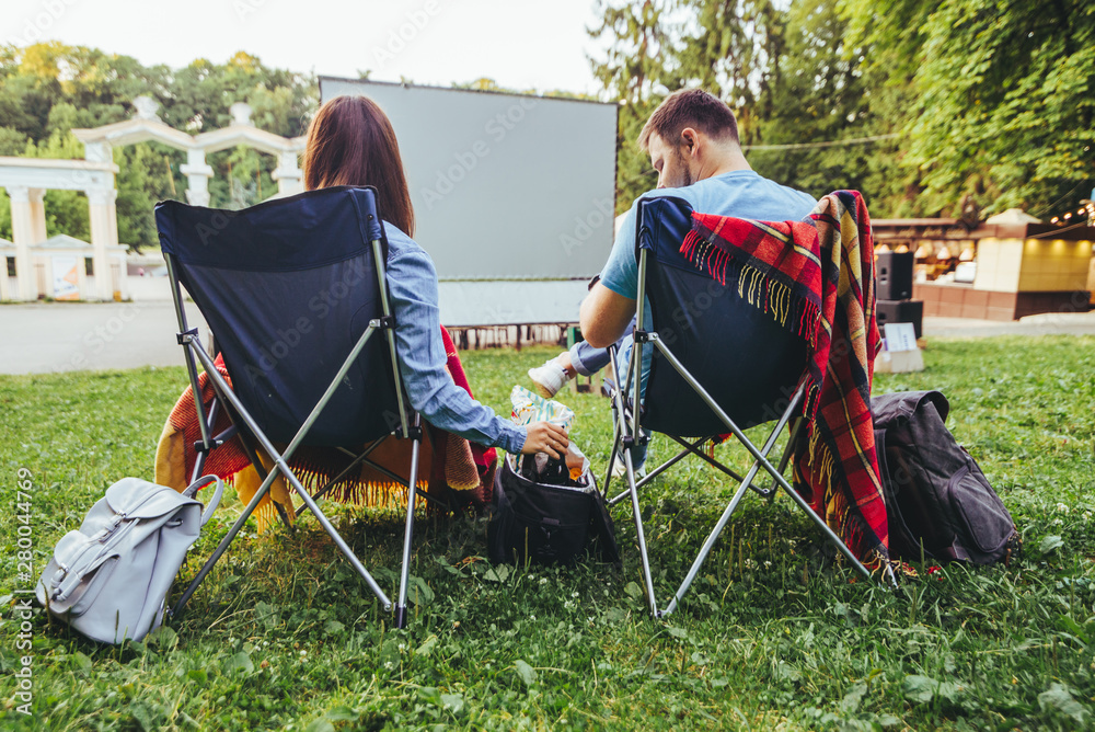 couple sitting in camp-chairs in city park looking movie outdoors at open air cinema couple sitting in camp-chairs in city park looking movie outdoors at open air cinema