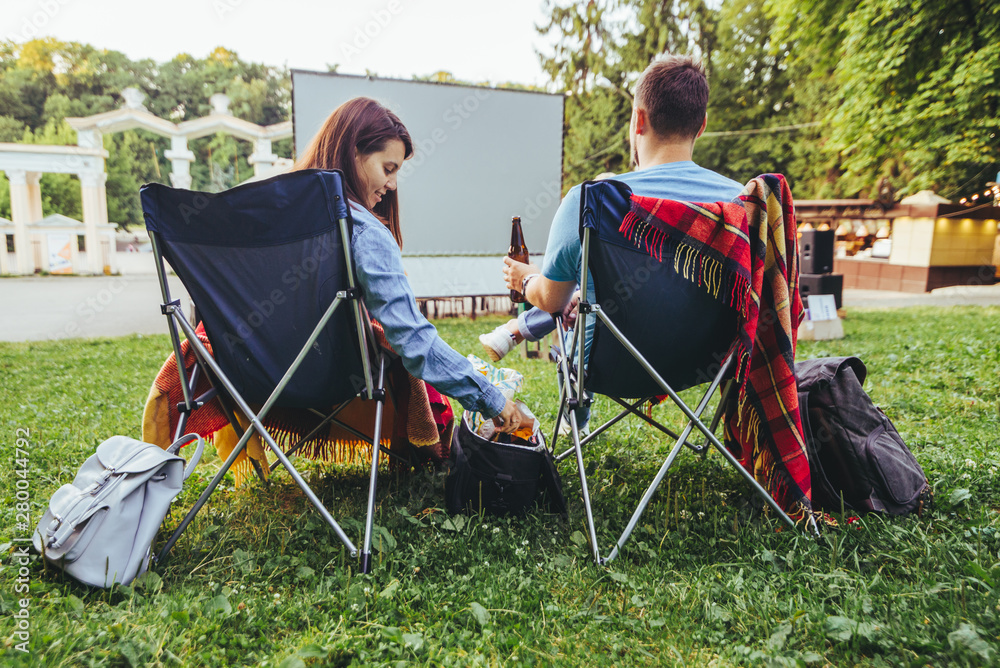 couple sitting in camp-chairs in city park looking movie outdoors at open air cinema couple sitting in camp-chairs in city park looking movie outdoors at open air cinema