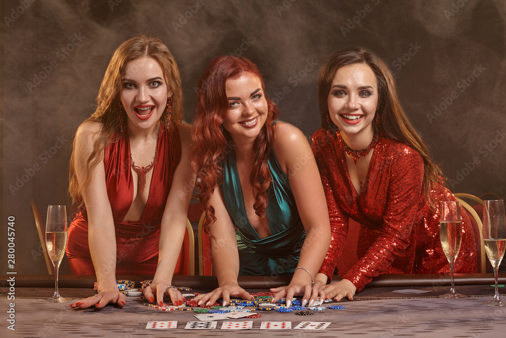 Three beautiful young women are playing poker at a casino.