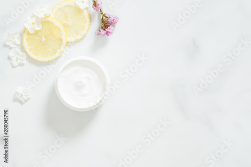 White moisturizing cream with lemon citrus and flower petals on marble background. Skin care beauty treatment with jar of body moisturizer. Bio organic, natural beauty products concept.