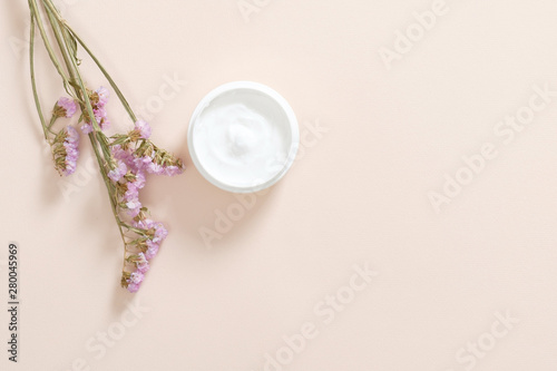 Jar with moisturizing body cream and dry flower on pastel pink background. Skin care cosmetic  anti aging concept. Minimal flat lay style composition  top view  copy space.