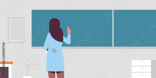 arab female school teacher standing in front of green chalk board rear view woman in traditional clothes writing on chalkboard education concept modern classroom interior flat portrait horizontal