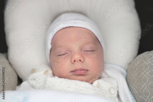 Close up of a baby sleeping in a pram. Little boy of some few months resting peacefully in a cold day. Baby carriage with pad for newly born. He is clothing with clothes.