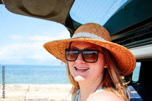 A woman weraing sunglasses and a hat in the summer car on the beach and ocean view..