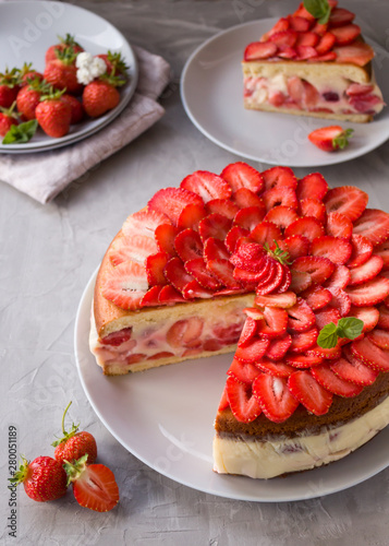 Cut biscuit cake with strawberries and vanilla jelly decorated with strawberry slices and mint leaves on a gray background. Fraisier cake .Vertical orientation, side view.