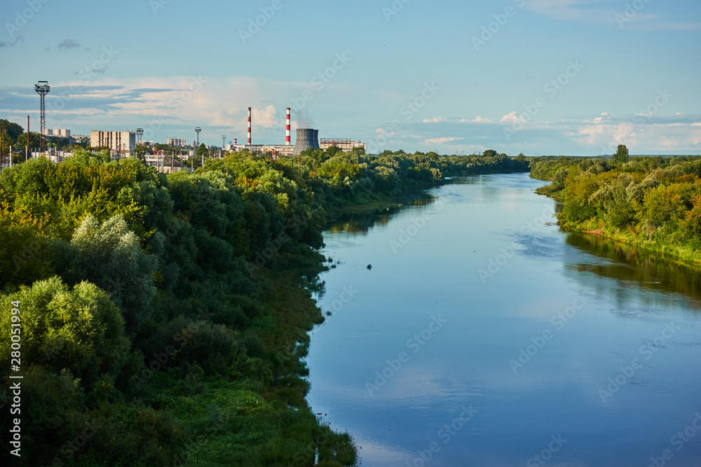 Wide river with forest and industrial buildings in the background