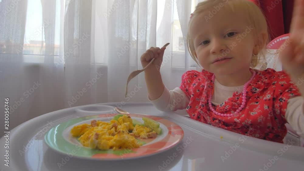 A cute little girl eating scrambled eggs in a baby chair A cute little girl eating scrambled eggs in a baby chair