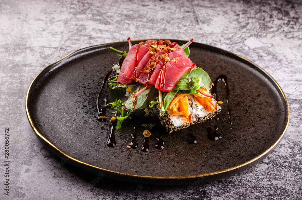 Close up of sashimi sushi set with raw tuna steak, avocado, cucumber and cheese philadelphia and soy on elegant black plate on concrete background. Modern Japanese food menu. Close up of sashimi sushi set with raw tuna steak, avocado, cucumber and cheese philadelphia and soy on elegant black plate on concrete background. Modern Japanese food menu.