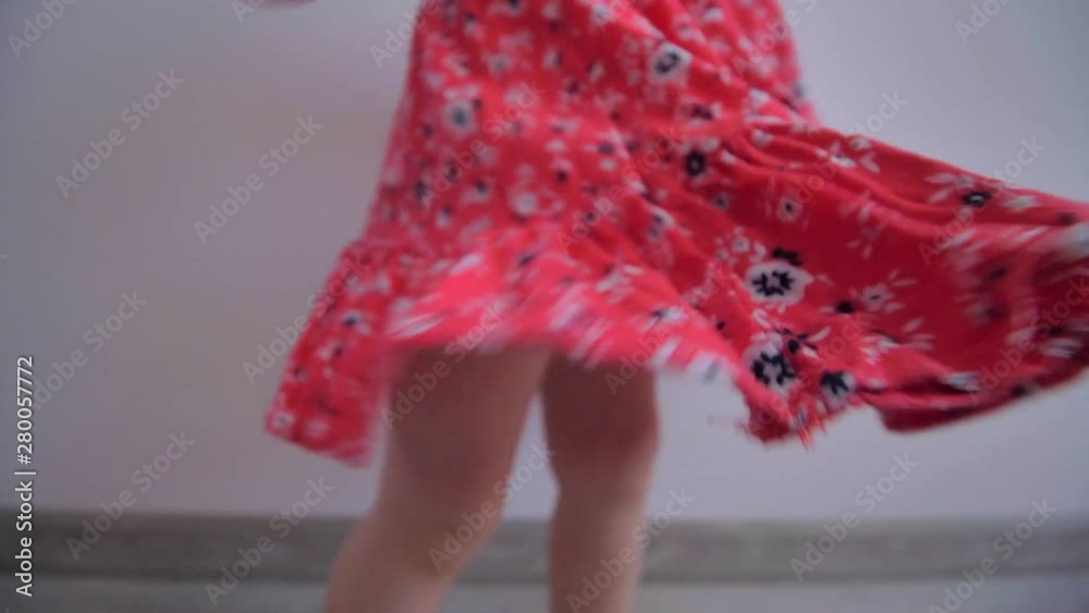 A little blond girl with a red dress is spinning and dancing