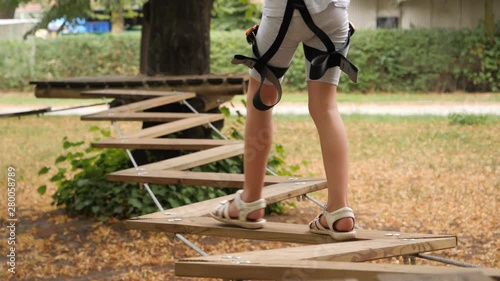 Rope park active child girl overcomes obstacles on suspended bridges of ropes and wooden boards photo