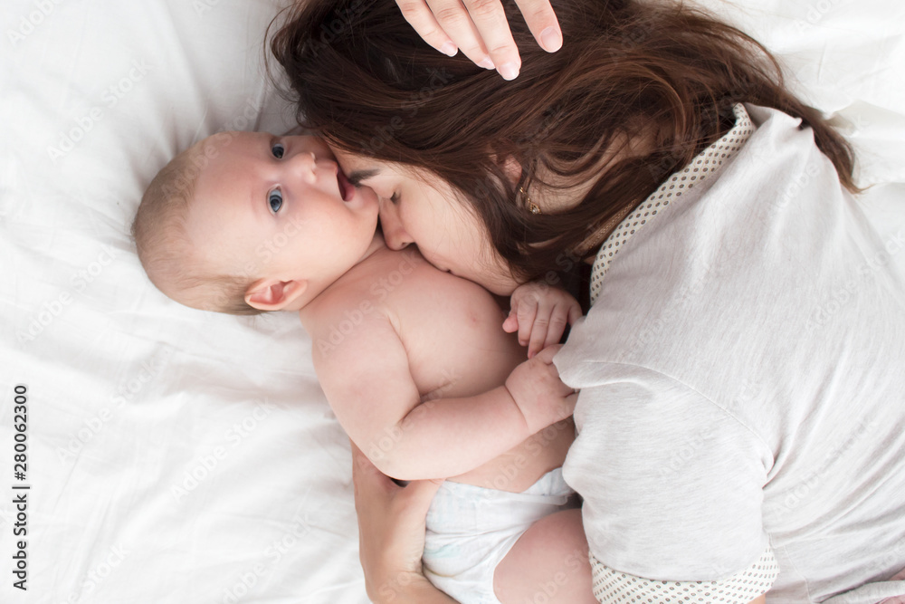 A brunette woman kisses a baby. Mom with baby closeup A brunette woman kisses a baby. Mom with baby closeup