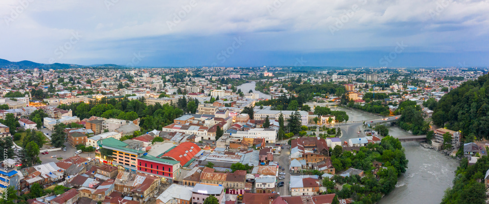Panoramic summer view of the city of Kutaisi, Georgia. Blue sky with clouds. River Rioni and old houses with Red roofs. Mountains in the distance.