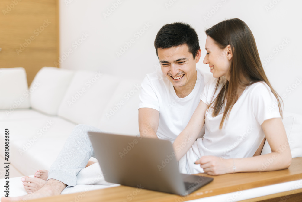 Happy young couple laughing at funny joke relaxing on sofa with laptop. Cheerful family enjoy holiday with notebook. Joyful man and woman enjoying sincere laughter having fun with computer at home Happy young couple laughing at funny joke relaxing on sofa with laptop. Cheerful family enjoy holiday with notebook. Joyful man and woman enjoying sincere laughter having fun with computer at home