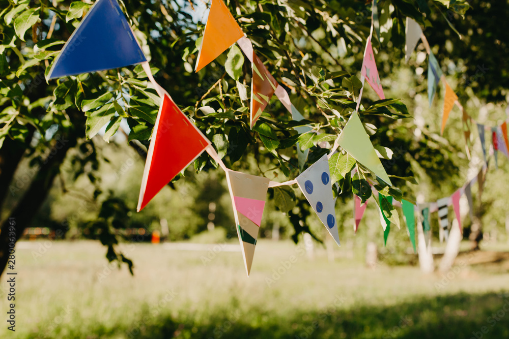 Multi-colored festive flags hang on a tree in the park. Picnic, holidays, birthday.