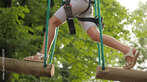 Rope park active child girl overcomes obstacles on suspended bridges of ropes and wooden boards photo