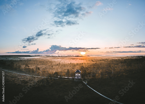  Warmly colored sunrise over a foggy swamp. Aerial view of stunning landscape at peat bog at Cenas Tirelis in Latvia. Wooden trail leading along the lake surrounded by pounds and forest.  photo