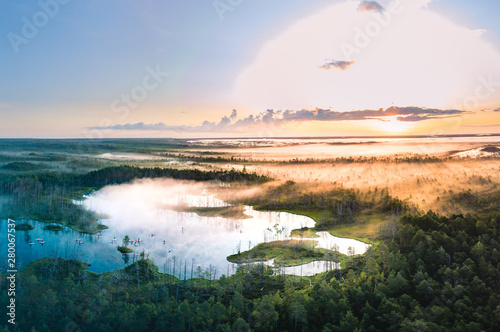  Warmly colored sunrise over a foggy swamp. Aerial view of stunning landscape at peat bog at Cenas Tirelis in Latvia. Wooden trail leading along the lake surrounded by pounds and forest.  photo