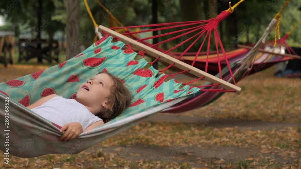 Little child girl has fun rest lying swaying fail almost falling from hammock in a park Little child girl has fun rest lying swaying fail almost falling from hammock in a park