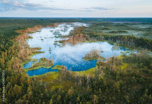 Warmly colored sunrise over a foggy swamp. Aerial view of stunning landscape at peat bog at Cenas Tirelis in Latvia. Wooden trail leading along the lake surrounded by pounds and forest.  photo