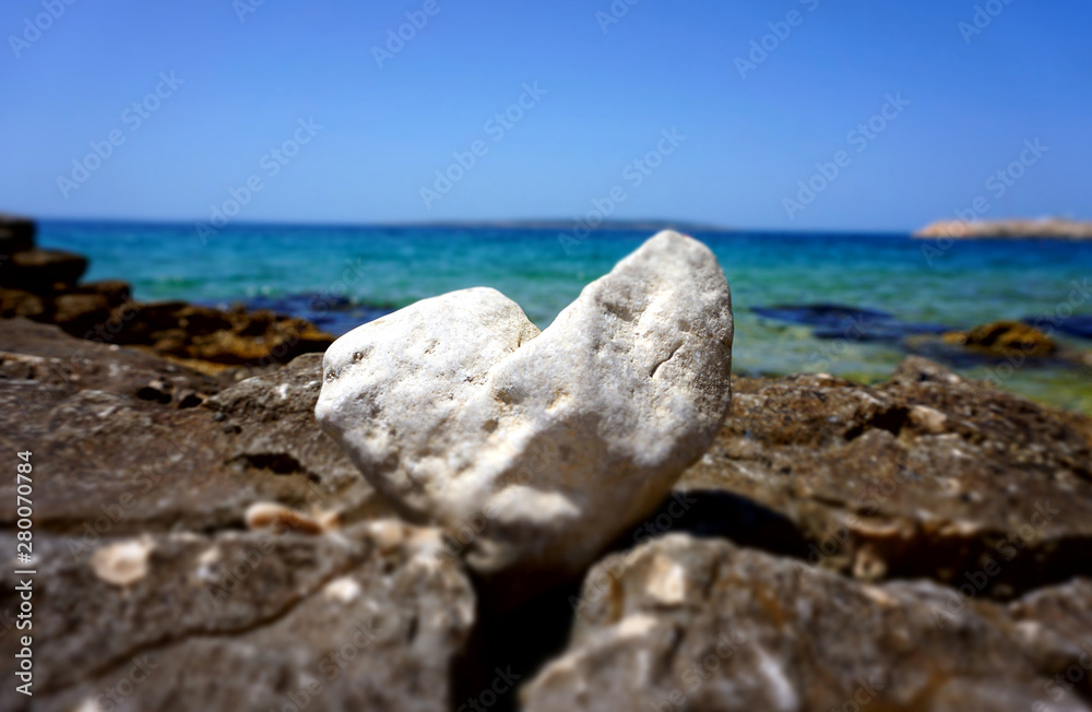 Beautiful summer background with a white heart shaped stone in front of the beautiful blue sea and sky horizon line