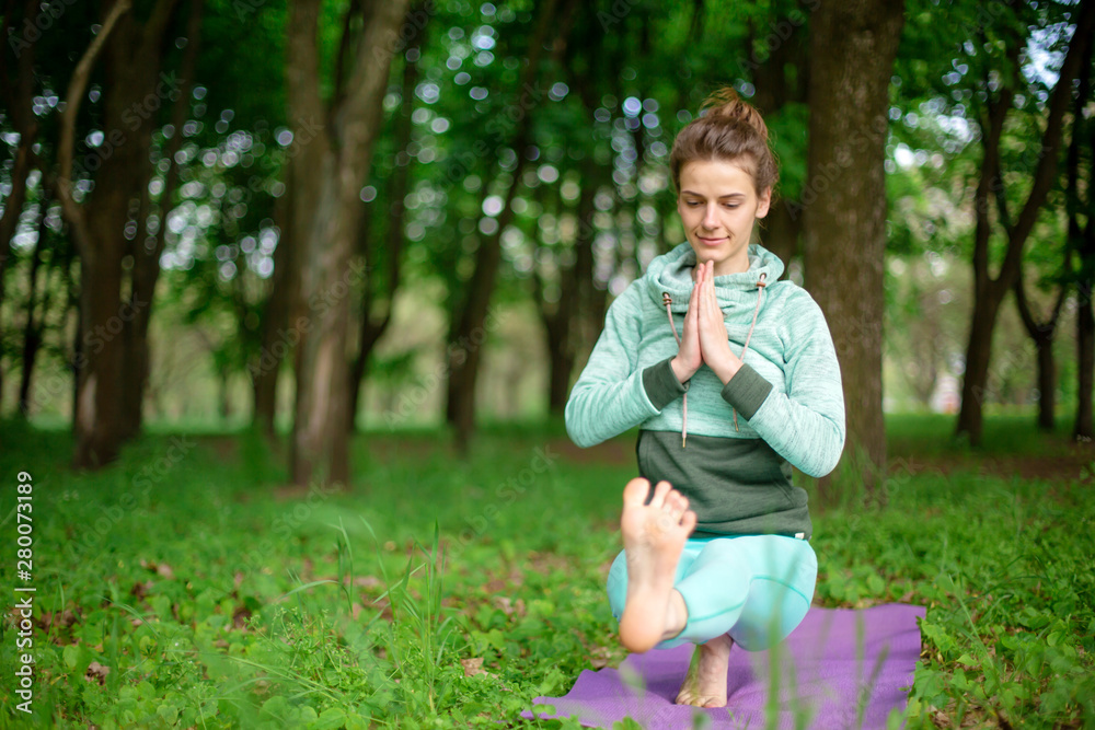 Thin brunette girl plays sports and performs beautiful and sophisticated yoga poses in a summer park. Green forest on the background. Woman doing exercises on the yoga mat, foot forward close-up Thin brunette girl plays sports and performs beautiful and sophisticated yoga poses in a summer park. Green forest on the background. Woman doing exercises on the yoga mat, foot forward close-up