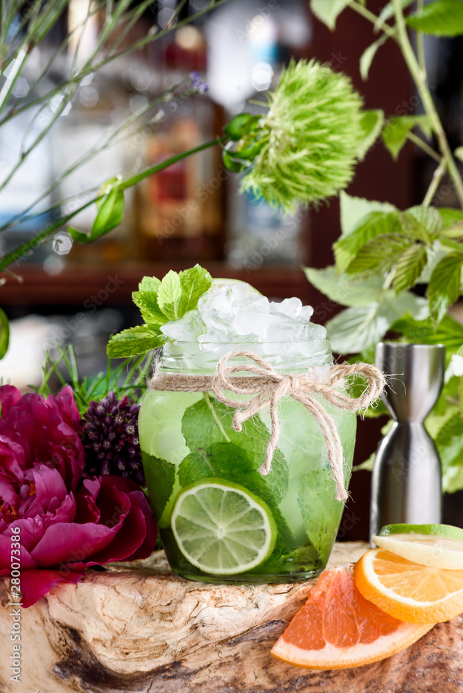 Cucumber lemonade with ice and slices of cucumber and lime in beautiful round glass on the background of fresh flowers