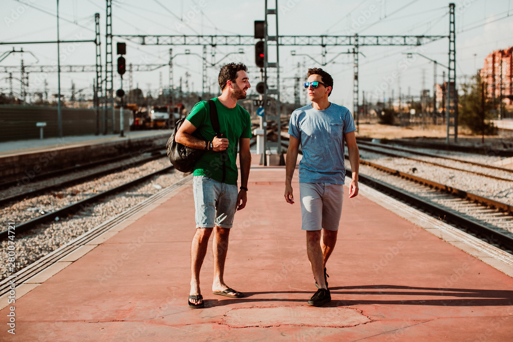.Two brothers on the platform waiting for the train. Relaxed and happy about to start their vacation. Lifestyle. Travel photography