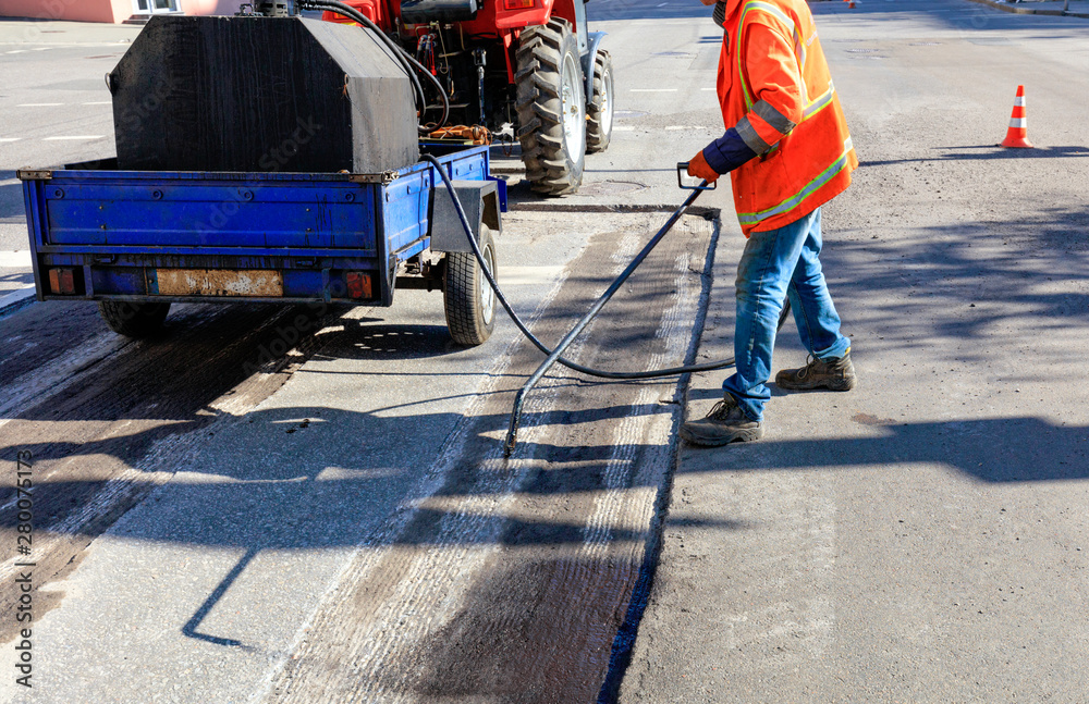 Worker repairs part of the asphalt road, spraying bitumen on the asphalt surface.