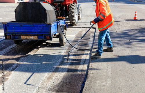 Worker repairs part of the asphalt road, spraying bitumen on the asphalt surface.