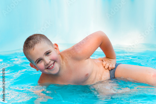 happy little boy relaxing in pool with turquoise water in summer vacation