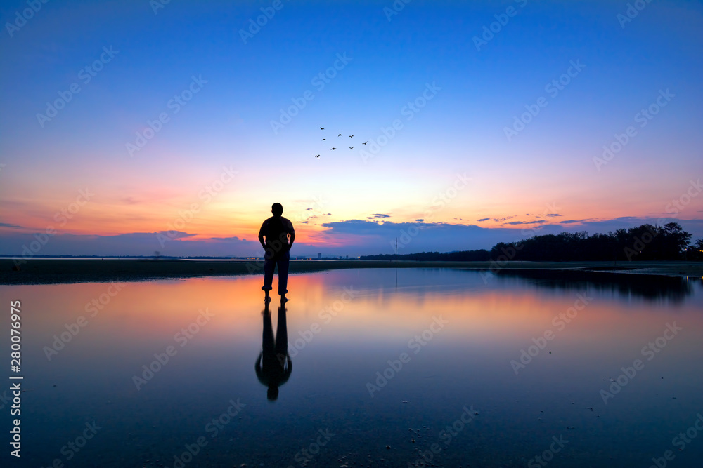 Silhouette of a men looking to the birds flying during sunset