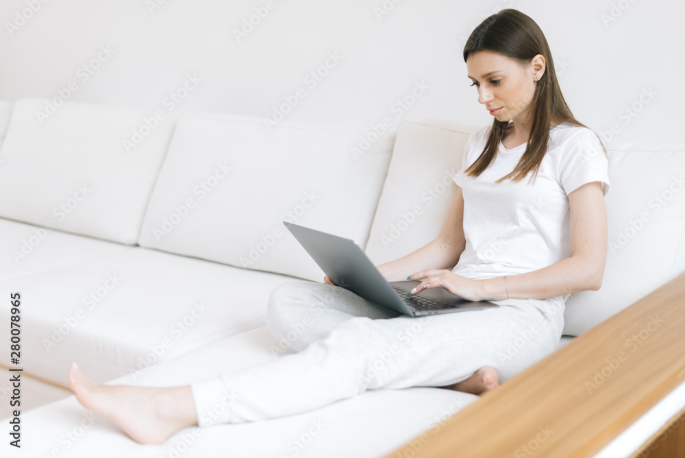 Serious young woman think on ideas for development of own website sitting on soft comfortable sofa in light home. Girl blogger typing on laptop computer in bright modern living room Serious young woman think on ideas for development of own website sitting on soft comfortable sofa in light home. Girl blogger typing on laptop computer in bright modern living room
