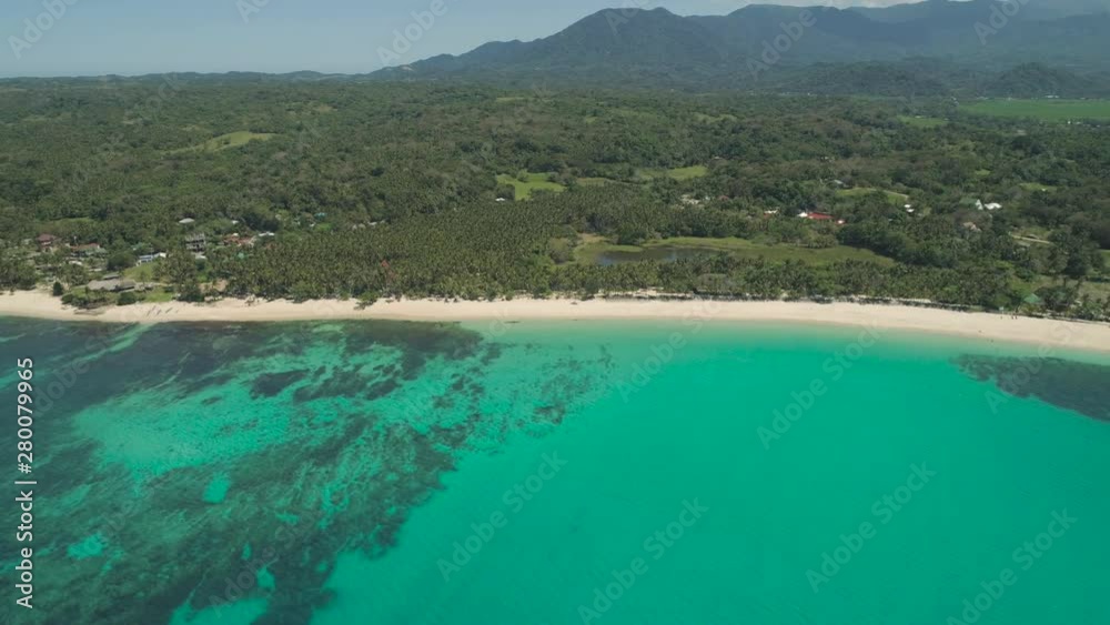 Aerial view of beautiful tropical beach Saud with turquoise water in blue lagoon, Pagudpud, Philippines. Ocean coastline with sandy beach and palm trees. Tropical landscape in Asia.