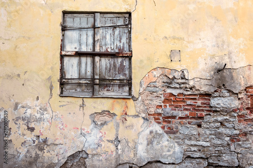 old wooden shutters close the window in the brick wall with peeling stuccoed shabby plaster. photo