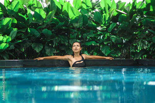 Portrait of young sexy caucasian woman in swimming pool with green plants