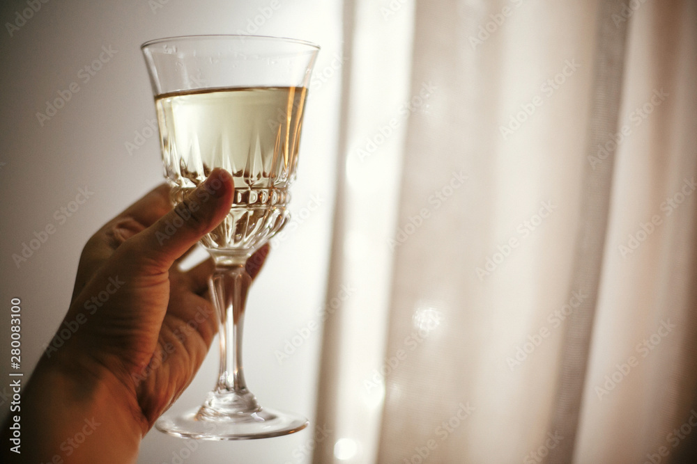 Obraz premium Hand holding champagne glass on background of christmas lights, celebrating and toasting in festive room. Space for text. Happy New Year eve party. Happy Holidays