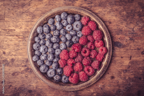 Delicious ripe blueberry and raspberry berries as a symbol of yin and yang in a metal plate on a rustic wooden table close-up, top view