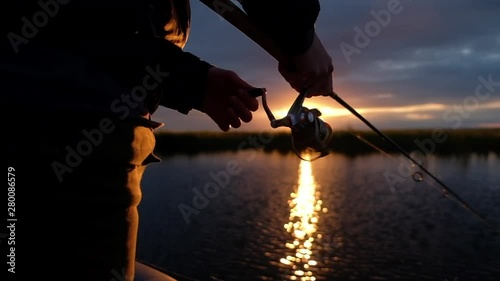 Fisherman spins the fishing reel on the lake at sunset