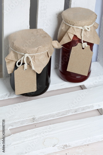 Jars of jam, covered with paper and tied with twine. On the string hang craft labels. Stand in a wooden box.