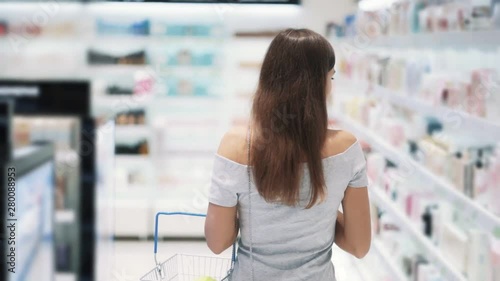 Backside view, girl shopping in cosmetics store with basket, slow motion