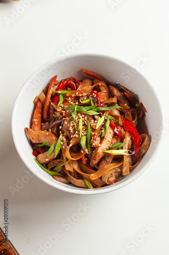Wheat thick wok noodle with roasted bell pepper, soy sauce, chicken, carrot and sesame on white background