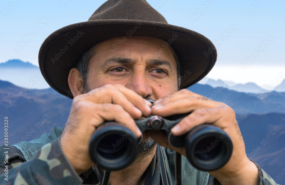 Obraz premium A hunter in a hat with binoculars looks out for prey.