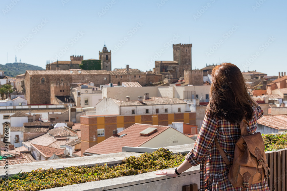 A young red-haired tourist with a backpack observes the old town of Caceres from the viewpoint of Galarza