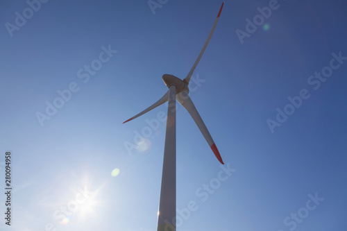 wind turbine with sun flare blue sky background view from below