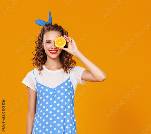 cheerful young curly woman girl with orange on yellow background.cheerful young curly woman girl with orange on a yellow color background.