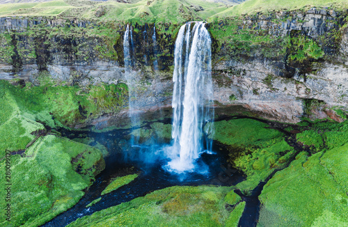 Iceland. Fantastic view of Seljalandsfoss waterfall. Water flow at covered with green grass cliff background. Iconic travel destination. Green color in Northern nature. Landscape photography.