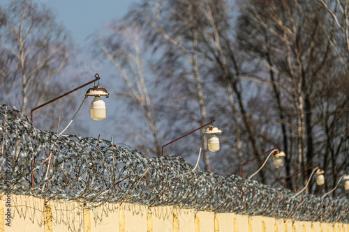 Barbed wire on a concrete fence with outdoor lamps. Limited depth of field. photo